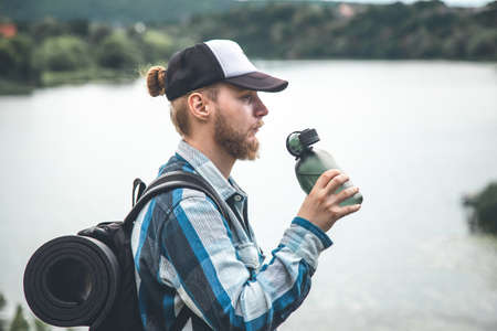 A man traveler with a backpack and a karemat keeps drinking water from a flask.の写真素材