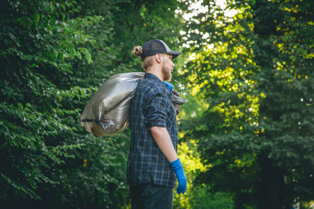 A young man in gloves and with a garbage bag cleans up in the forest.の写真素材