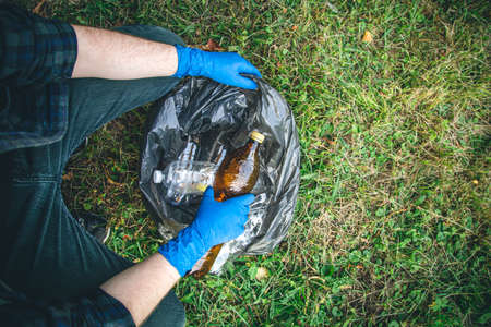 A man cleans up the forest, throws a bottle into a trash bag, close-up.の写真素材