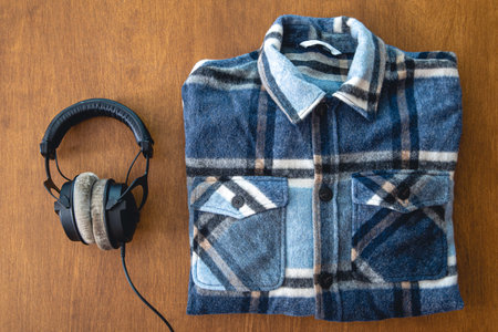 Headphones and a folded plaid shirt on a wooden background.