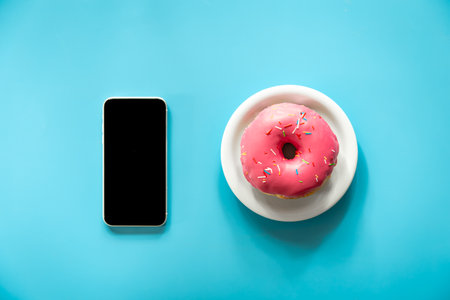 Donut with pink icing and a smartphone on a blue background.の写真素材