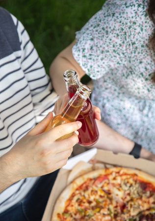 A young man and woman drink drinks in glass bottles at a picnic.の写真素材