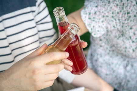 A young man and woman drink drinks in glass bottles at a picnic.