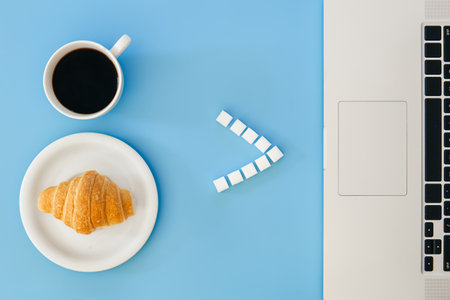 Croissant, cup of coffee and laptop on a blue background, flat lay.の写真素材