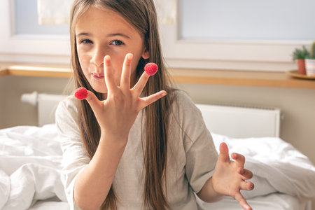 Funny little girl with raspberries on her fingers in bed in the morning.