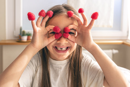 Funny little girl with raspberries on her fingers in bed in the morning.の写真素材