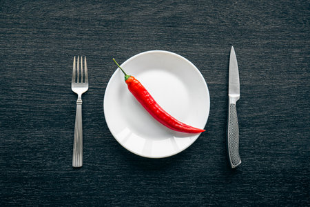 Flat lay, chili peppers on a white plate and cutlery on a black background.の写真素材