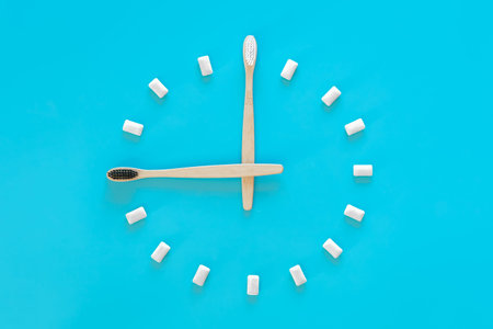 Flat lay, a clock made of chewing gum on a blue background and a toothbrush.