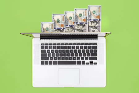 Laptop and dollar bills on color background, flat lay.