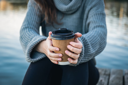 Close-up, a cup of coffee in the hands of a woman in nature near the river.の写真素材