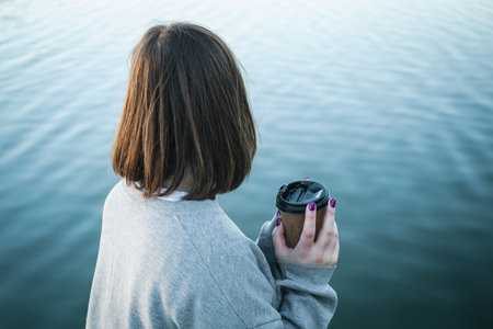 A young woman with a cup of coffee on the background of the river.の写真素材
