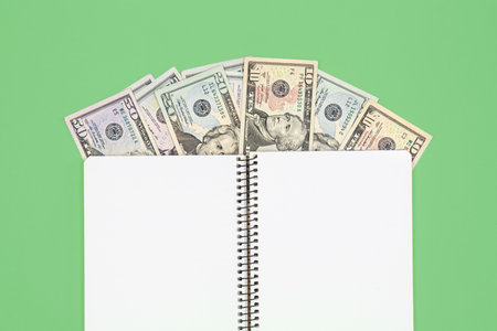 Opened blank notepad and dollar bills on green background, flat lay.の写真素材