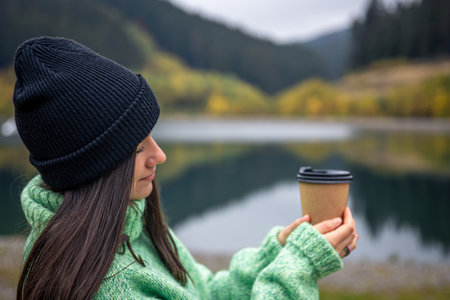 A young woman with a cup of coffee on a blurred background of mountains.の写真素材