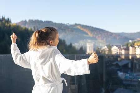 A little girl in a bathrobe on the balcony of a hotel in the mountains.の写真素材