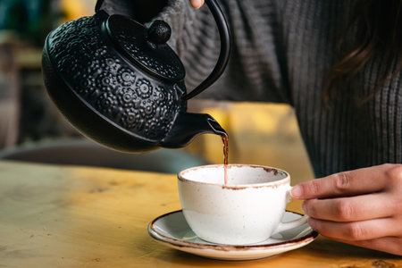 Woman in a cafe pour tea from a black cast iron teapot.の写真素材