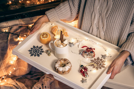 A cup of cocoa with marshmallows and decor details on a tray in female hands.の写真素材