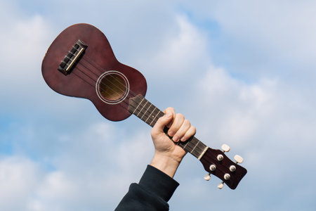 Guitar ukulele in man hand against cloudy sky, nature blurred background.