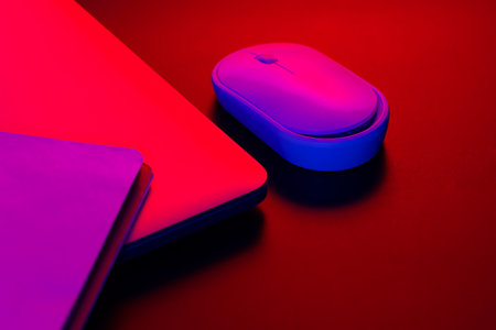 Computer mouse near a laptop in neon lighting, close-up.の写真素材