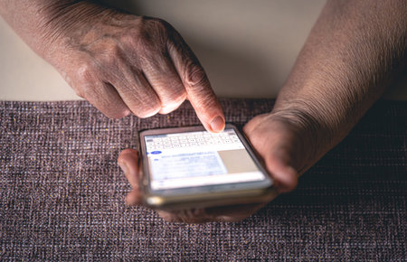 Hands of an elderly woman holding a mobile phone, close up.