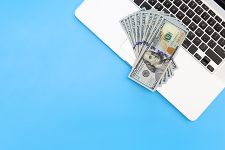 Dollar bills on a laptop on a blue background, flat lay, copy space.の写真素材