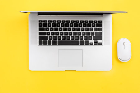 Laptop and computer mouse on yellow background, flat lay, workplace concept.の写真素材