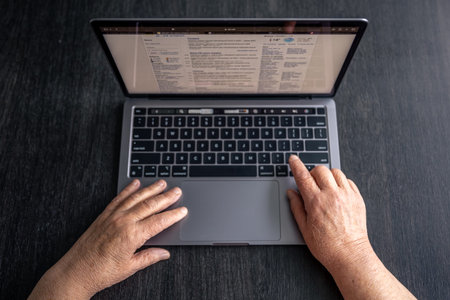 Aged woman uses laptop, top view, old hands close up, old generation and technology concept.