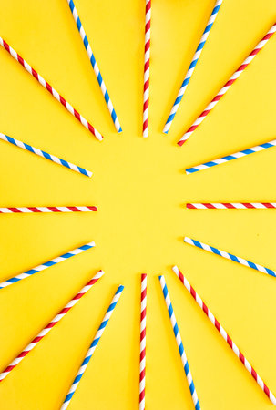 Multicolored party drinking straws arranged into a circle on yellow background, top view, copy...