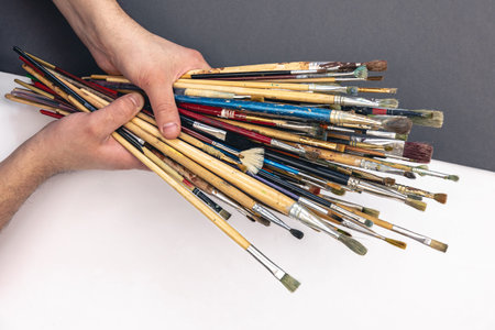 A lot of brushes for drawing in male hands on a colored paper background, top view.