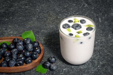 A glass of yogurt with blueberries on a black background, close-up.の写真素材