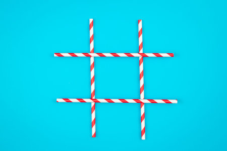 A tic-tac-toe board game made of paper drinking straws on a blue background, flat lay, copy space.