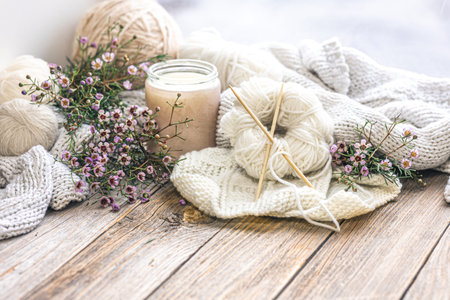 Cozy home composition with knitting threads, knitting needles, a candle and flowers close-up on a...