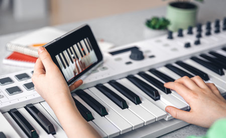 A child learns to play the piano with a smartphone, online music lesson, self-study with the help of...