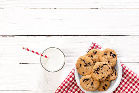 Plate with chocolate chip cookies, and a glass of milk on a wooden background, flat lay.の写真素材