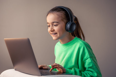 Funny little girl in headphones with laptop plays games, game addiction concept.の写真素材