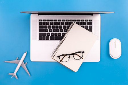 Laptop, notepad and airplane miniature on a blue background, concept of searching for air tickets and tourism.の写真素材