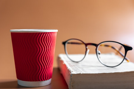 Glasses, a book and a paper glass of coffee.の写真素材