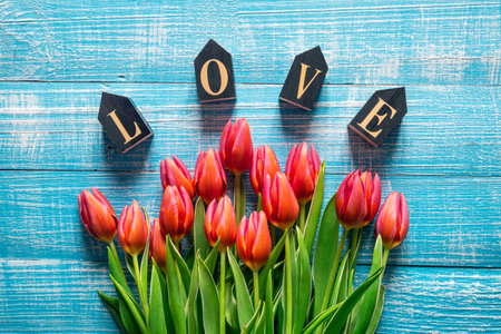 Bouquet of tulips and decorative word love on a wooden background, top view.の写真素材