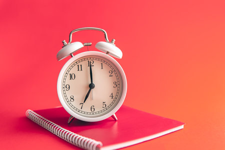 White alarm clock and notebook on Viva Magenta background.の写真素材