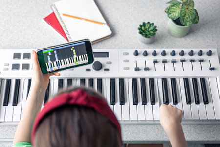 A little girl learns to play the piano with a smartphone, online music lesson.の写真素材