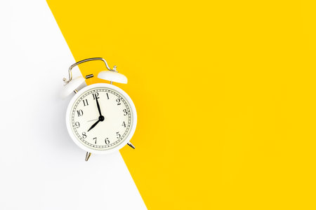White alarm clock on a white and yellow background, flat lay.の写真素材