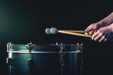 A man plays a musical percussion instrument with sticks on a dark background.の写真素材