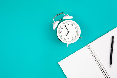 Notebook and alarm clock on a blue background, flat lay.