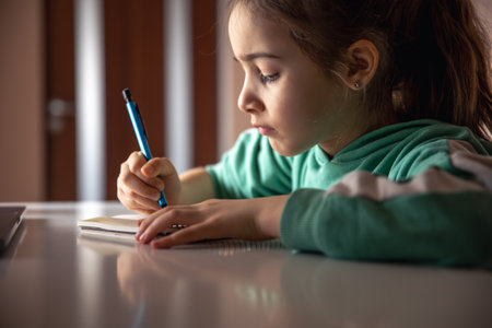 Serious little girl writes with a pen in a notebook.の写真素材
