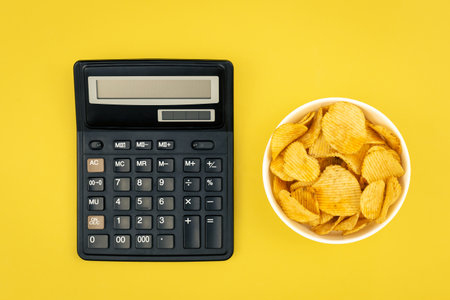 A plate of potato chips and a calculator on a yellow background, top view.の写真素材