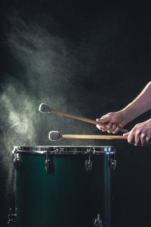 A man plays a musical percussion instrument with sticks on a dark background.の写真素材