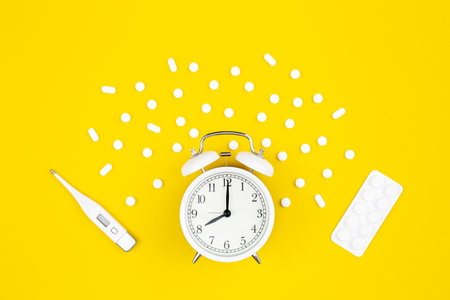 Alarm clock, medical thermometer and pills on a yellow background, flat lay.の写真素材