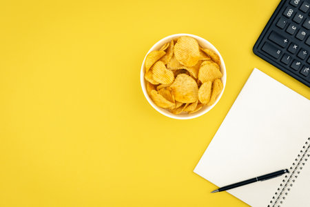 A plate of potato chips, a calculator and a notebook on a yellow background.の写真素材