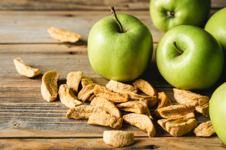Homemade dried organic apple and and raw green apples on a wood background.