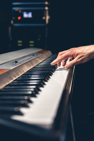 A mans hand plays the piano keys in a dark interior of a music studio.の写真素材