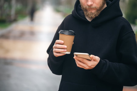 Man holding paper cup and smartphone outdoors.の写真素材